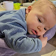 Milo participe au concours pour gagner de l'argent avec cette photo : baby, infant, child, towel, blanket, pillow, blue_clothing, face, cheek, hand, mouth, sleepy, close_up, portrait, indoors, table, mug, cup, soft_texture, cozy