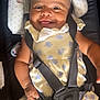 baby, child, smile, car_seat, seatbelt, headband, yellow_dress, floral_pattern, infant, happy, cute, tongue_out, sitting, strapped_in, indoors, closeup, face, skin, hand, footwear