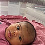 Angie is registered to the contest to win money with this photo: baby, infant, face, eyes, blanket, pink, mesh, playpen, indoor, window, brick_wall, curious, soft_texture, lying_down, child, person, head, closeup, newborn, cute