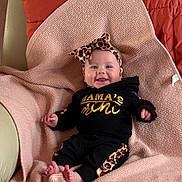 Kovie is registered to the contest to win money with this photo: baby, infant, smile, headband, leopard_print, black_clothing, blanket, pink_blanket, couch, cozy, happy, cute, indoors, portrait, child, feet, sitting, comfortable, fashion, headwear