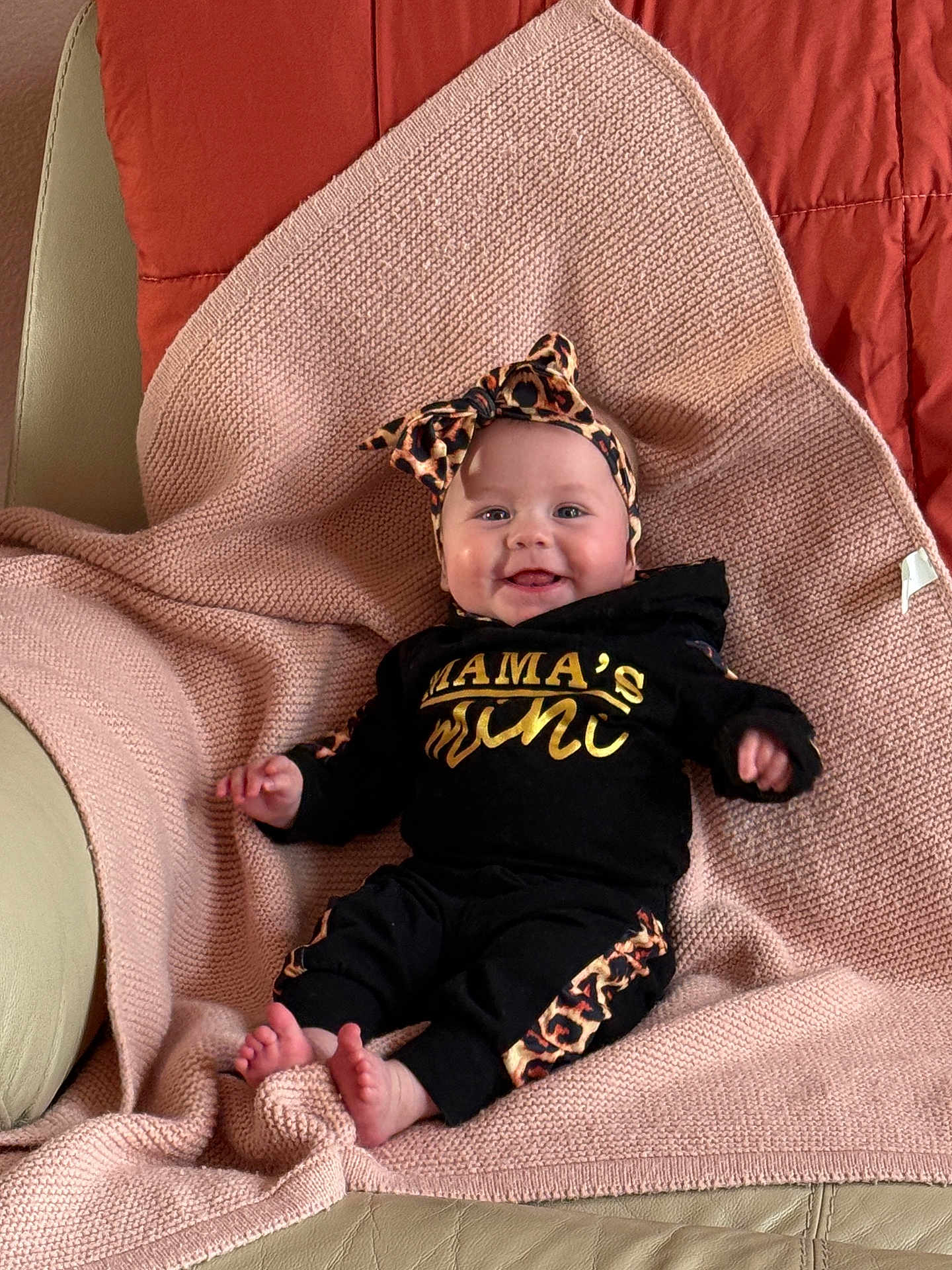 Kovie is registered to the contest to win money with this photo: baby, infant, smile, headband, leopard_print, black_clothing, blanket, pink_blanket, couch, cozy, happy, cute, indoors, portrait, child, feet, sitting, comfortable, fashion, headwear