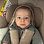 baby, child, car_seat, seatbelt, gray_sweater, face, infant, cushion, safety, indoors, head_support, clothing, straps, person, skin, looking_at_camera, cute, young_child, car_safety, warm