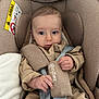 baby, infant, car_seat, child, seat_belt, safety_harness, blanket, clothing, hand, face, head, indoors, cushion, young_child, person, portrait, baby_clothes, seat, straps, comfort