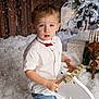 child, boy, white_shirt, red_bow_tie, rocking_horse, snow_effect, christmas_gifts, holiday_decor, reindeer_decoration, wooden_wall, festive, indoor, portrait, cute, winter_theme, holiday_photo, present, decorations, young_child, celebration