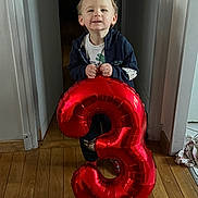 Jimy participe au concours pour gagner de l'argent avec cette photo : balloon, birthday, boy, casual_clothing, celebration, child, face, happy, holding, home, indoor, light, number_three, party, red, smile, smiling, standing, wooden_floor, young_child