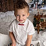 child, boy, smiling, white_shirt, red_bow_tie, winter, snow, holiday, christmas_gifts, decorations, wooden_wall, indoor, portrait, festive, happy, cute, seasonal, celebration, sitting, cozy