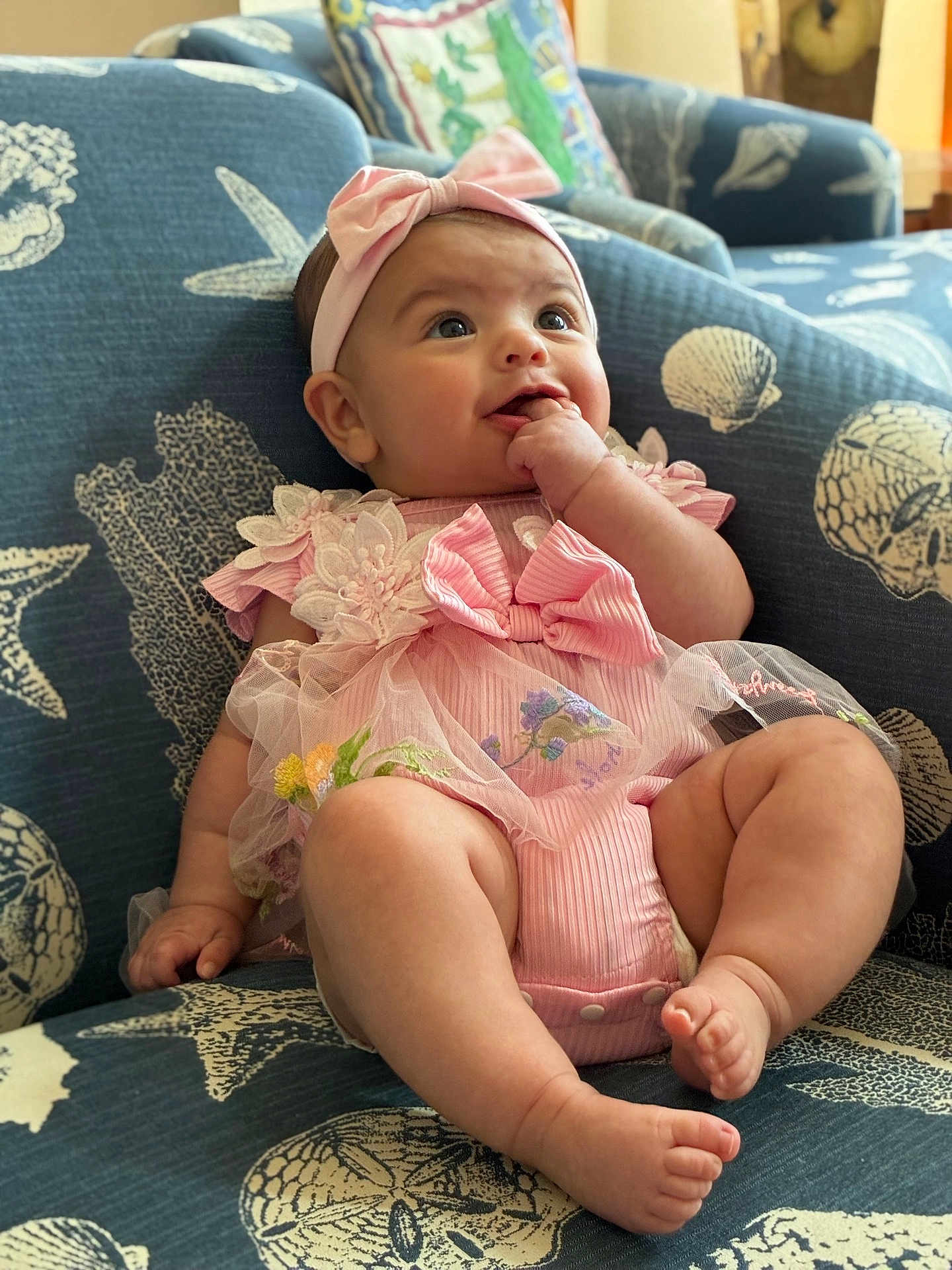 Sienna joined the competition — help win amazing prizes! baby, child, pink_outfit, headband, couch, seashell_pattern, starfish_pattern, indoor, cute, smiling, sitting, plush, furniture, happy, portrait, infant, hand, feet, clothing, person