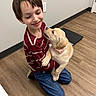 affection, blue_jeans, boy, casual_clothing, child, collar, cute, dog, embrace, floor, happy, indoor, kneeling, light_wall, pet, puppy, short_hair, smiling, striped_shirt, wooden_floor