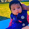 baby, blue_sky, casual_wear, child, clothing, cute, daytime, grass, hand, infant, nature, outdoor, patches, person, portrait, sitting, sunlight, support, trees, vest