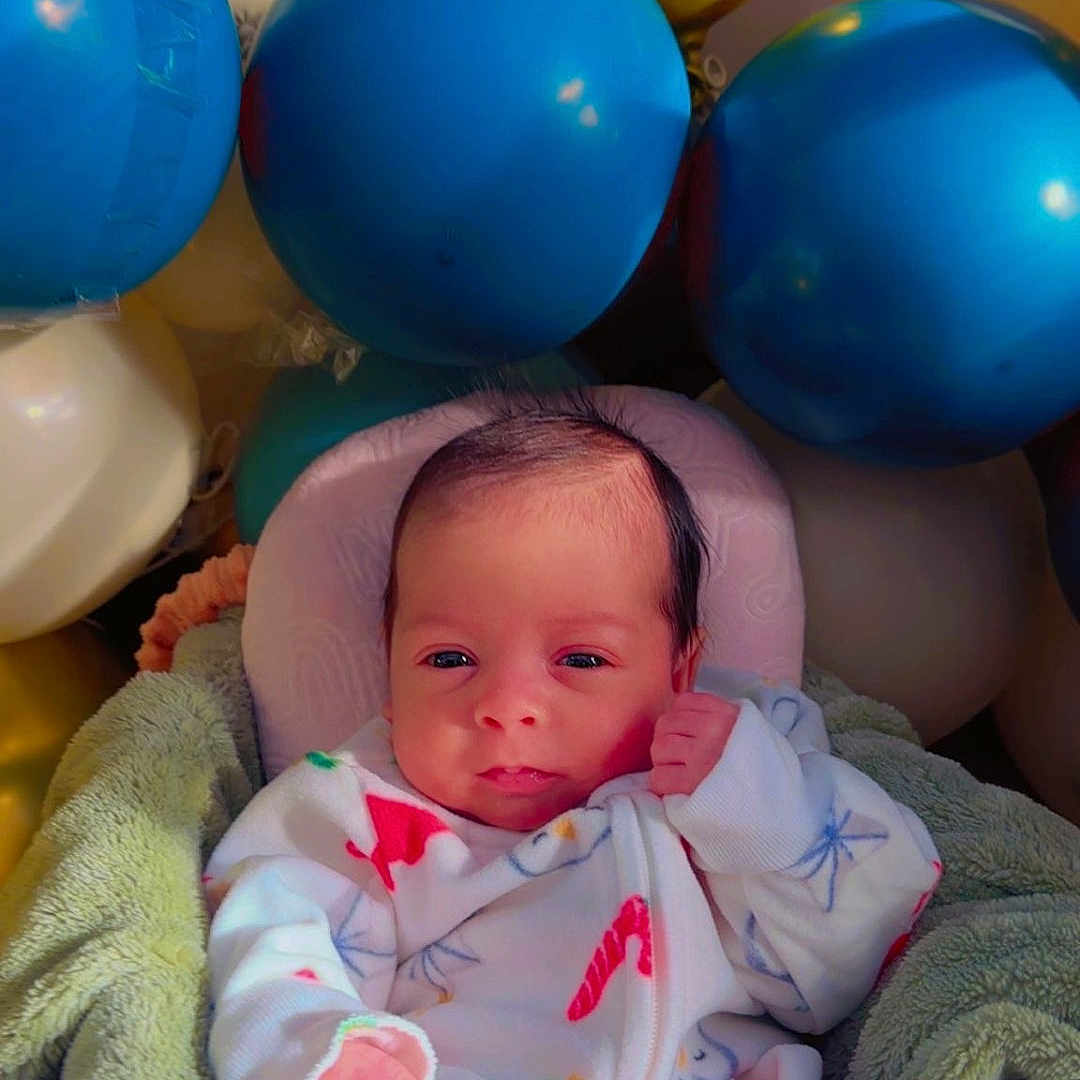 Taim is registered to the contest to win money with this photo: baby, balloons, blanket, blue_balloons, celebration, child, colorful, cozy, cream_balloon, cute, face, gold_balloon, hand, indoor, infant, newborn, pajamas, portrait, smiling, soft