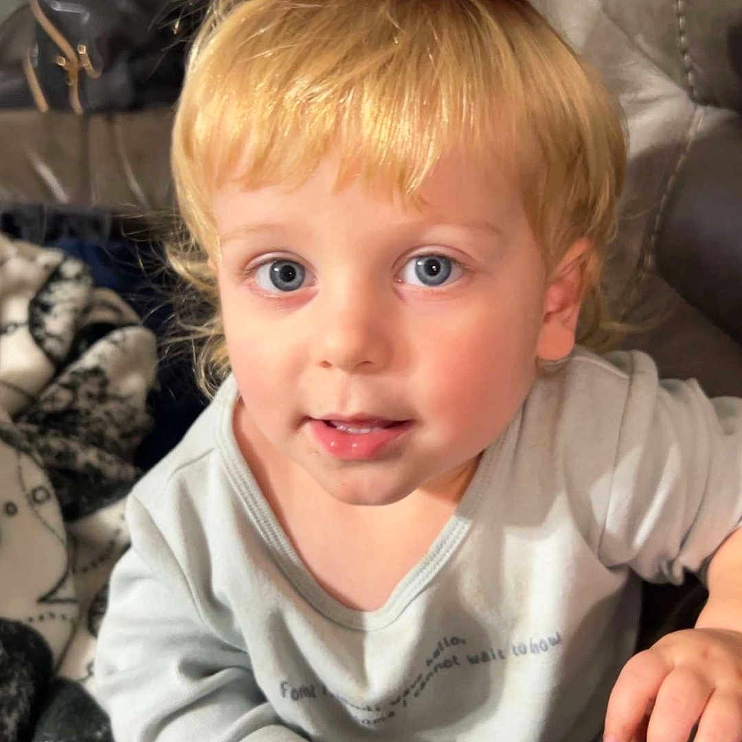 Jon is registered to the contest to win money with this photo: blanket, blonde_hair, blue_eyes, casual_clothing, child, couch, cowboy_hat, cute, expression, face, hand, home, indoor, person, playful, portrait, seated, small_hat, toddler, young_child