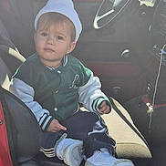 Santino a rejoint le concours — aidez-le/la à gagner de superbes lots ! toddler, child, white_beanie, green_jacket, sneakers, car_interior, car_seat, steering_wheel, window, sunlight, casual_clothing, young_child, portrait, sitting, curious_expression, indoor, vehicle, footwear, casual_style, daylight