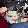 Alva is registered to the contest to win money with this photo: baby, sunglasses, pacifier, car_interior, steering_wheel, cow_print, child, infant, seat, clothing, hand, person, casual, car_door, window, reflection, seatbelt, jeans, button, cute