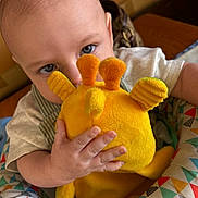 Alva joined the competition — help win amazing prizes! baby, child, plush_toy, yellow_toy, blue_eyes, curious, hand, infant, seated, patterned_seat, indoor, close_up, soft_toy, cute, small_hand, face, person, colorful, comfortable, playful