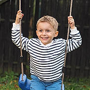 Miliano participe au concours pour gagner de l'argent avec cette photo : active, blue_swing, boy, casual_clothing, child, daylight, fence, fun, grass, happy, leisure, nature, outdoor, playground, portrait, ropes, short_hair, smiling, striped_shirt, swing