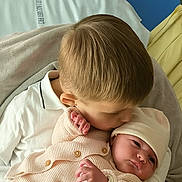 Milana a rejoint le concours — aidez-le/la à gagner de superbes lots ! baby, bed, blanket, child, comfort, cuddle, family, hat, indoor, infant, kiss, knitted_clothing, love, newborn, person, portrait, sibling, soft_texture, tenderness, warmth