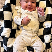 Pyper joined the competition — help win amazing prizes! baby, infant, smiling, face, hand, blanket, checkered, black_and_white, clothing, floral_pattern, cute, lying_down, happy, infant_clothing, plush, newspaper, floor, portrait, indoor, cozy