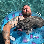 Maximus is registered to the contest to win money with this photo: man, dog, french_bulldog, pool, inflatable_ring, tattoo, relaxing, water, sunny, pet, swimming, summer, outdoor, panting, beard, closed_eyes, floating, blue, fun, leisure