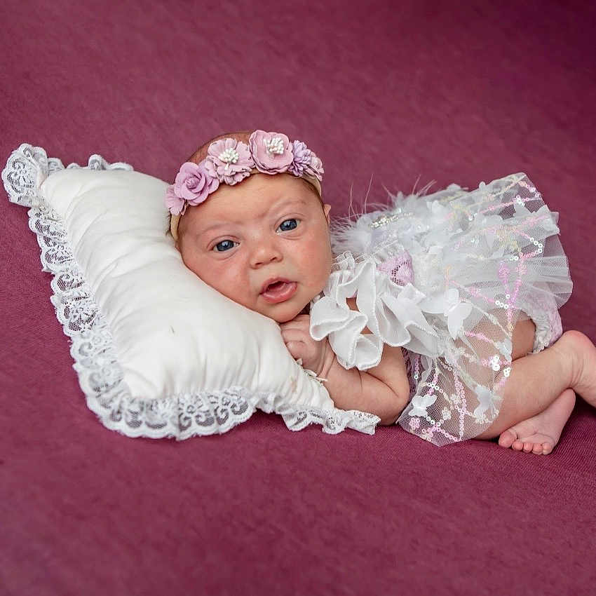 Kinsley joined the competition — help win amazing prizes! baby, infant, pillow, flower_crown, white_clothing, lace, purple_background, newborn, portrait, cute, lying_down, sparkles, headband, small_feet, soft_texture, resting, child, studio_photo, adorable, innocent