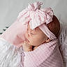 newborn, baby, pink_bow, headband, blanket, sleeping, infant, cushion, soft_texture, portrait, cute, child, wrapped, peaceful, resting, indoors, closeup, adorable, young, toddler