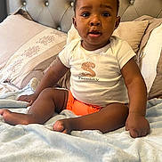 Liam joined the competition — help win amazing prizes! baby, child, toddler, bed, blanket, pillow, white_tshirt, orange_shorts, indoor, home, cute, sitting, portrait, face, skin, head, expression, furniture, cozy, soft