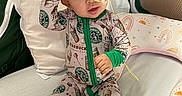 Anahi is registered to the contest to win money with this photo: baby, child, onesie, headband, pink_bow, starbucks_logo, feeding_tube, bed, pillow, blanket, footwear, green_trim, cute, indoor, infant, sitting, expression, curious, person, cozy