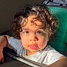 Noah is registered to the contest to win money with this photo: toddler, child, curly_hair, playful, sunlight, tongue_out, face, portrait, expression, indoors, shirt, skin, person, hand, cute, baby, young_child, light, shadow, background