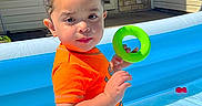 Noah is registered to the contest to win money with this photo: toddler, child, pool, inflatable_pool, toy, green_ring, orange_shirt, blue_shorts, water, backyard, door, brick_wall, sunny, outdoor, summer, play, fun, person, young_child, daytime