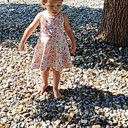 Juliette joined the competition — help win amazing prizes! toddler, child, barefoot, floral_dress, outdoor, pebbles, sunlight, shadow, tree_trunk, fence, nature, curious, young_child, summer, daylight, skin, standing, person, casual, playful