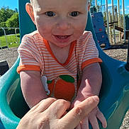 Bryson is registered to the contest to win money with this photo: baby, blue, child, clothing, cute, daylight, grass, hand, happy, infant, orange, outdoor, person, play_equipment, playground, sky, smile, sunlight, swing, trees
