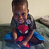 Steve Williams is registered to the contest to win money with this photo: child, smiling, spiderman, plush_toy, bed, blanket, indoor, casual_clothing, person, happy, sitting, young, cute, toy, portrait, home, comfortable, brown_skin, short_hair, tshirt
