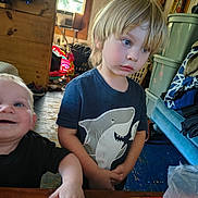 Adeline is registered to the contest to win money with this photo: baby, toddler, child, siblings, smiling, portrait, indoors, family, shark_shirt, blue_eyes, blond_hair, standing, sitting, toys, laundry, storage_bins, blankets, wooden_room, casual_clothing, photograph
