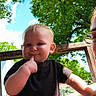 baby, child, outdoor, portrait, sitting, smiling, black_shirt, colorful_shorts, finger, cheek, face, person, adult, glasses, backyard, trees, leaves, blue_sky, sunlight, wooden_railing