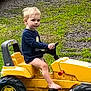 Blake joined the competition — help win amazing prizes! child, blonde_hair, barefoot, toy_vehicle, yellow, outdoor, grass, gravel, long_sleeve_shirt, sitting, vehicle, play, kid, casual, daylight, young, bare_legs, small, foot, person
