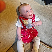 Ruby is registered to the contest to win money with this photo: baby, infant, smiling, sitting, couch, red_clothing, white_clothing, knitted, happy, face, hand, legs, tights, indoor, furniture, cute, child, portrait, looking_away, expression