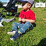 Baha participe au concours pour gagner de l'argent avec cette photo : child, toddler, boy, grass, outdoor, sunny, cap, red_tshirt, blue_pants, sneakers, stroller, person, park, daytime, nature, greenery, sitting, casual_clothing, young_child, side_profile