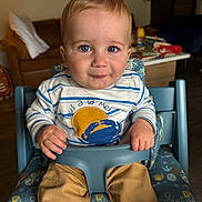 Milo a rejoint le concours — aidez-le/la à gagner de superbes lots ! baby, child, toddler, high_chair, blue_eyes, striped_shirt, crab_design, pants, rolled_up_pants, indoor, couch, cushions, table, toys, person, face, hands, smile, furniture, home