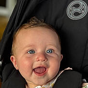 Jasmin is registered to the contest to win money with this photo: baby, child, smiling, blue_eyes, stroller, black, clothing, floral, pattern, ear_piercing, face, happy, infant, cute, person, portrait, sitting, closeup, baby_girl, indoors