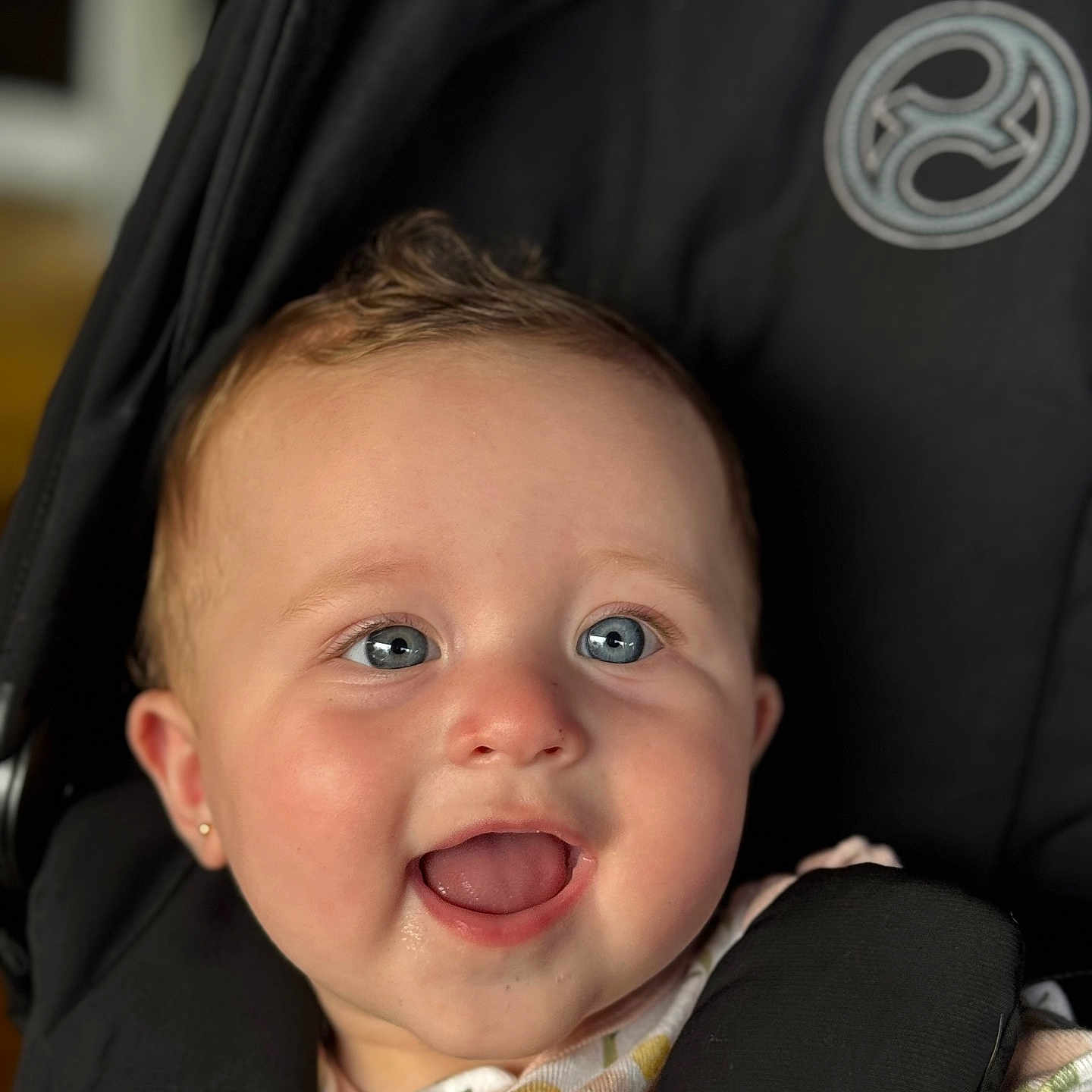 Jasmin is registered to the contest to win money with this photo: baby, baby_girl, black, blue_eyes, child, closeup, clothing, cute, ear_piercing, face, floral, happy, indoors, infant, pattern, person, portrait, sitting, smiling, stroller