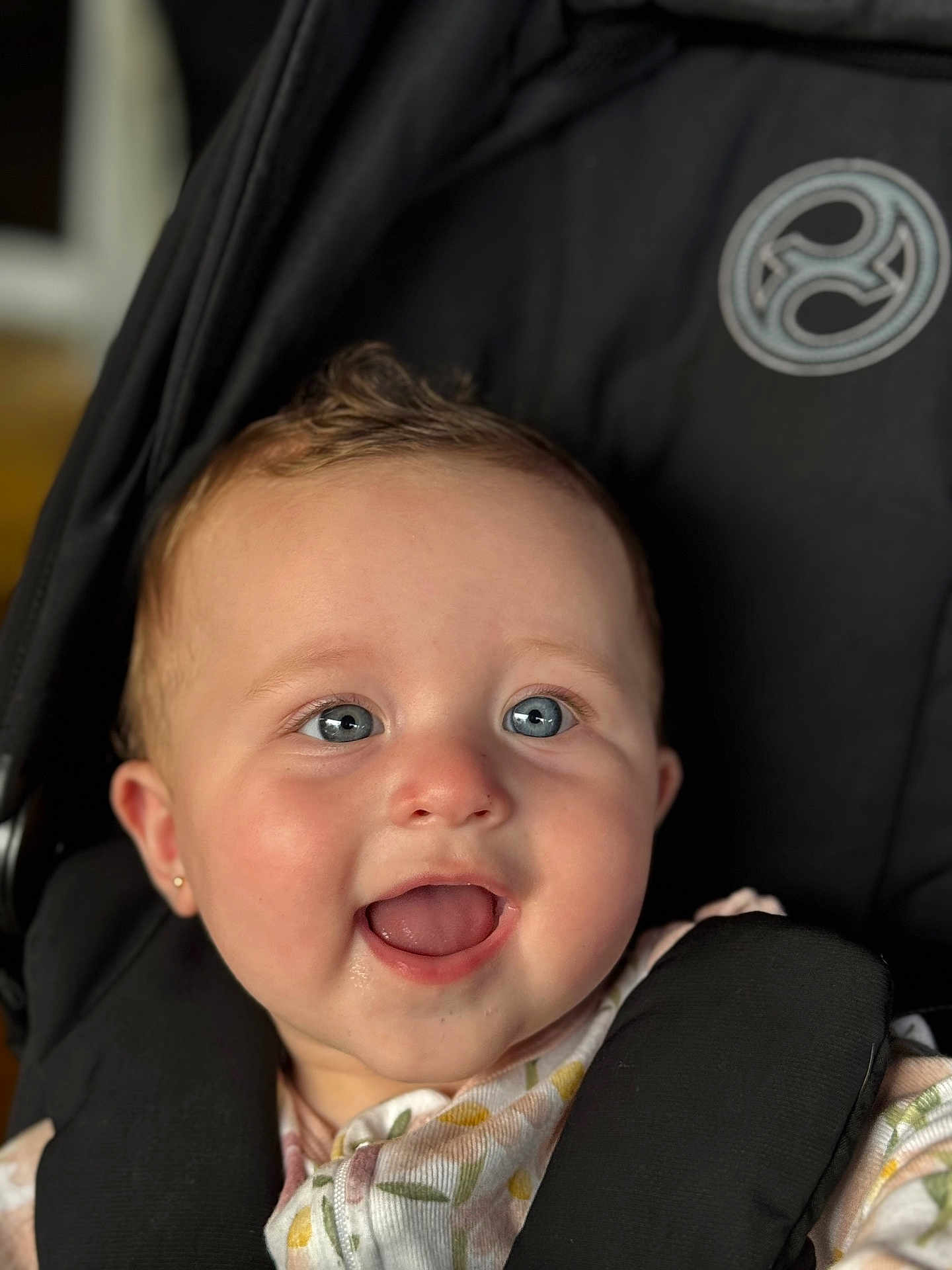 Jasmin is registered to the contest to win money with this photo: baby, child, smiling, blue_eyes, stroller, black, clothing, floral, pattern, ear_piercing, face, happy, infant, cute, person, portrait, sitting, closeup, baby_girl, indoors