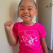 Legacy is registered to the contest to win money with this photo: child, smiling, standing, pink_shirt, white_shorts, bracelet, beads, hair_beads, indoor, door, carpet, happy, person, casual_clothing, portrait, young_child, joy, fashion, cute, wall