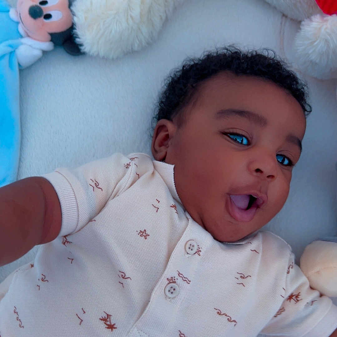 Eli-Nathan a rejoint le concours — aidez-le/la à gagner de superbes lots ! baby, blanket, child, clothing, comfort, curly_hair, cute, happy, indoors, infant, lying_down, mickey_mouse, playful, plush_toy, portrait, resting, short_sleeves, smiling, soft_texture, young_child