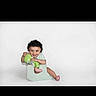 child, toddler, baby, sitting, potty_chair, smiling, curly_hair, green_clothing, pink_shoes, portrait, studio, white_background, indoor, infant, playful, happy, cute, seated, photography, throne