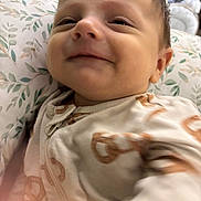 Cohen is registered to the contest to win money with this photo: baby, child, close_up, cozy, cute, expression, face, happy, indoor, infant, pajamas, pattern, pillow, portrait, resting, sleepwear, smile, soft_lighting, young_child, zipped_clothing