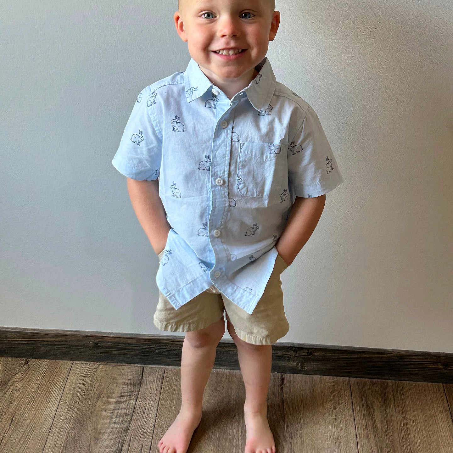 Grayson is registered to the contest to win money with this photo: child, boy, smile, barefoot, shorts, shirt, standing, hands_in_pockets, wooden_floor, indoor, light_blue, bunny_prints, casual_clothing, happy, portrait, young_child, cute, casual_pose, wall, floor