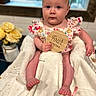 baby, child, infant, blanket, flower, vase, window, wooden_sign, face, person, clothing, sitting, cute, indoor, floral_pattern, skin, hand, foot, table, soft