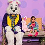Kobi is registered to the contest to win money with this photo: child, girl, easter_bunny, mascot, plush_toy, bench, purple_background, polka_dots, colorful_clothing, smiling, hair_beads, indoor, costume, playful, decorations, pink_shoes, toy, happy, seated, fun