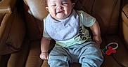 Braelin is registered to the contest to win money with this photo: baby, child, smiling, sitting, portrait, leather_chair, armchair, indoor, home, clothing, bib, pants, socks, toy, happy, face, curly_hair, furniture, cozy, photograph