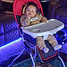 baby, infant, child, high_chair, sitting, portrait, face, looking_up, hand, hoodie, clothing, white_shoes, tray, stroller, living_room, couch, carpet, indoor, blue_lighting, neon_lighting