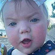 Gabriella is registered to the contest to win money with this photo: baby, child, face, close_up, bow, headwear, dress, stars_pattern, outdoor, daylight, sky, person, expression, curious, summer, nature, tree, beach, hand, cute
